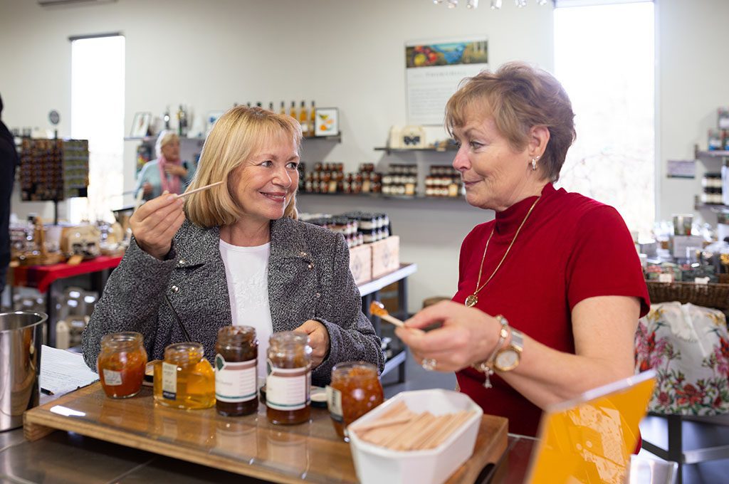 Two older women smiling and dipping popsticks into the preserves bottles