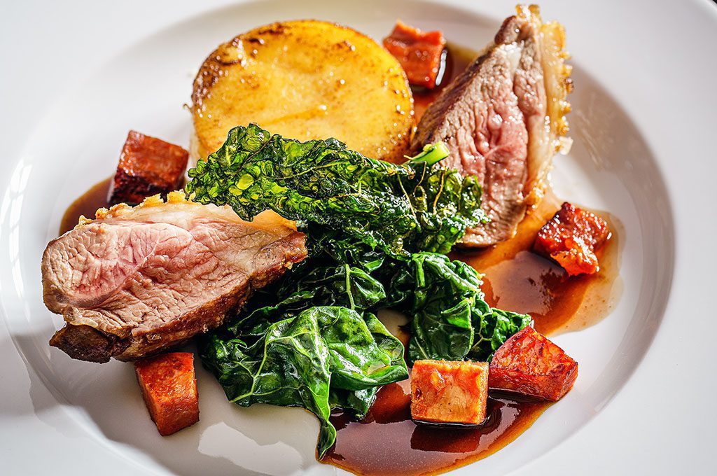 Duck breast sitting in a white bowl with roast vegetables
