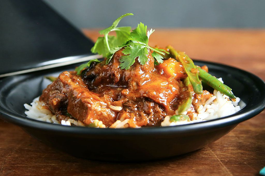 Moroccan chicken in a black bowl with white rice and a sprig of coriander on top