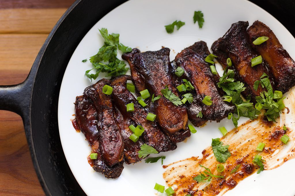 Pork ribs on a white plate with brown sauce and chives