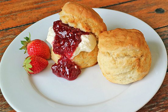 White plate that has two scones. One scone is cut open and has jam and cream in it